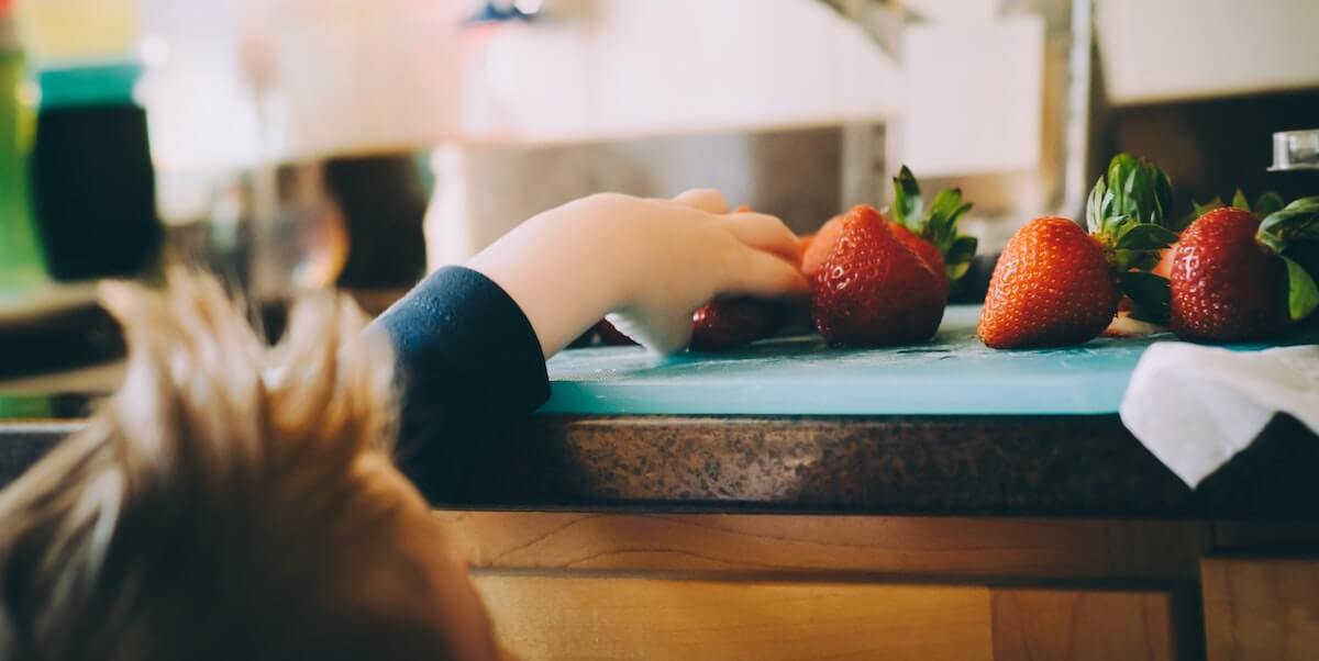 kid reaching for strawberries on counter